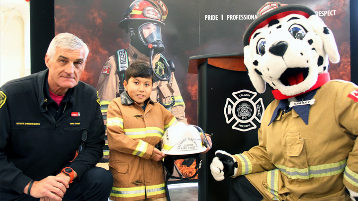 Calgary Fire Department's Fire Chief Steve Dongworth appoints Mustafa Mohammadi as Junior Fire Chief as Sparky the mascot watches on.